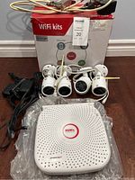 Full kit displayed with cameras, base station, cables, and power adapters against a wooden floor background.