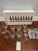 Nine assorted wine glasses arranged in front of boxed wine rack and wine tools on wooden surface
