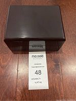 Closed dark wooden box with maxsold auction label marked '48 Women's Watch' beneath it on wooden floor.