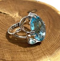 Close-up side view of ring showing large oval blue faceted stone and openwork band design.