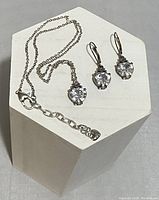 Silver-tone chain necklace with clear crystal heart pendant, matching crystal heart earrings with lever-back hooks on white display stand.