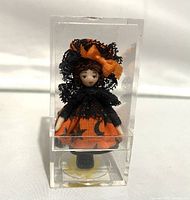 Front view of miniature Halloween Hilda doll wearing an orange and black Halloween dress with stars and moons, displayed in a clear acrylic box about 2.3 inches tall.