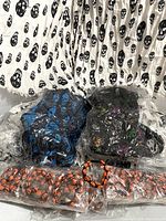 Photo showing skull pattern scarves in white with black skulls, blue skull scarves, multi-colored skull scarves, and the wrapped orange skull bead bracelets.