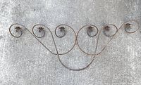 Front view of the large iron wall candelabra laying on concrete showing six curled candle arms and rusted iron finish.