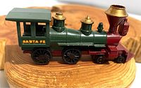 Side view of vintage Lesney Models of Yesteryear train engine. Green and red metal model with gold detailing and 'Santa Fe' marking, placed on wooden surface.