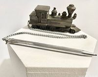 Side view of metal locomotive paperweight with attached mechanical pencil on chain, showing engraved 'ROGERS' on the side.