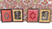 Two vintage photographic portraits with their respective hinged cases open, showing red patterned fabric and gold-colored picture frames.