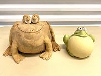 Front view of the large brown textured pottery frog planter and smaller green cream pottery frog planter with bulging eyes and wide openings.