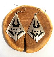 Front view of pair of diamond-shaped silver earrings with black geometric inlay on wooden background, showing design details and wear.