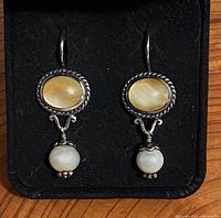 Front view of both sterling silver dangle earrings showing yellow oval stones and white round beads on black background.