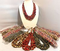 Photo showing the variety of multicolor bead necklaces fanned out around a white bust stand, with several necklaces inside clear plastic wrappers and several loose, displaying colors and shapes.