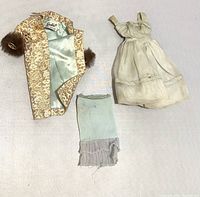 Three vintage Barbie clothing items consisting of a gold brocade jacket with satin lining, an off-white sheer sleeveless dress, and a light blue sock with ruffled cuff.