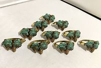 Front view showing grape cluster and leafy design with green patina on gold-tone napkin rings.