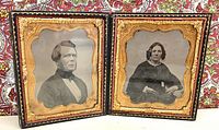 Pair of vintage portraits in an old hinged frame with ornate gold borders, sitting open against a patterned background.