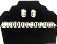 Full front view of bracelet and clip earrings on black display showing rhinestones and white accent bars