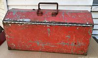 Photo of the closed red metal toolbox showing heavy wear and paint loss.