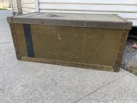 Whole view of the rectangular vintage army green metal trunk with riveted edges and black stripe.
