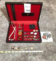 Overview of open black jewelry box showing red felt interior and assorted jewelry inside, plus front display of charms and necklaces