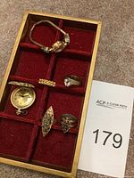Overview of six jewelry items arranged in red velvet tray including a wristwatch, pocket watch and four rings
