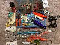 Overview of the fishing gear arranged on a plastic box lid including lures, pliers, hooks, and reels