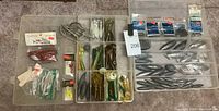 Overview of fishing tackle with lures, hooks, weights separated into compartments of two plastic tackle storage boxes.