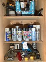Shelf with various spray paint and primer aerosol cans, and miscellaneous small tools and accessories below.