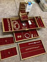 Wide view of large gold-tone jewelry box open displaying multiple pieces of costume jewelry in red velvet-lined trays.