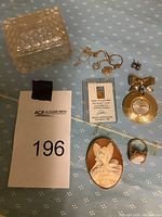 Overview of lot showing glass jewelry box, broken chains with heart charms, gold bar certificate card, brooch watch, cameo brooch and ring, and stud earrings