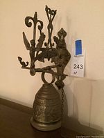 Full view of the 16 inch tall metal bell mounted on wall with an angel figure and candle holder, showing the bell and mounting bracket.