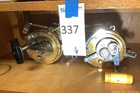 Front view of two gold Penn International reels with power handles (black and orange knobs)