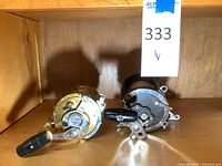 Two large reels side by side on wooden shelf beneath lot tag