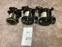 Three fishing reels laid out side by side on carpet showing front faces