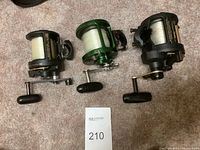 Overview of three baitcasting reels on carpet, each loaded with monofilament line