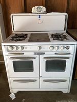 Front view of white enamel Wedgewood midcentury stove showing two ovens with glass doors, four burners on top, and chrome handles and control knobs.