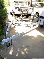 Full front-side view of the white trailer frame with rollers and hitch area, parked in driveway.