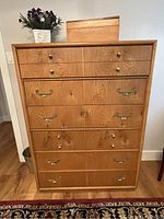 Tall wooden dresser with six large drawers and four smaller drawers on top, natural wood finish with brass and round knobs