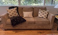 Front view of taupe corduroy upholstered sofa with three seat cushions, wooden legs, decorative pillows and throw.