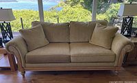 Front view of three-seat green-beige upholstered sofa with carved wood trim and cushions