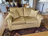 Front view of beige Ethan Allen loveseat with two matching beige cushions, sitting on a patterned rug in a living room with wood floors.