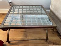 Top view showing square glass tabletop with grid metal design underneath and dark metal frame.