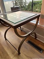 Side view of square glass top side table showing curved metal frame and support.