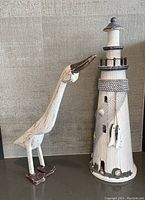 Photo showing two wooden decorative figurines: a lighthouse and a bird on a gray textured fabric background.