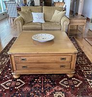 Square wooden coffee table with decorative bowl on top in front of sofa