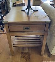 Front view of the wooden Nautica side table showing the drawer and slatted lower shelf next to a sofa.