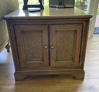 Nautica wooden side table with woven panel cabinet doors, round metal knobs, and a smooth top surface.