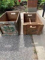 Two old wooden beverage crates placed side by side, showing worn paint and branding for Coke and Canada Dry.