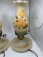 Single antique table lamp with cream opaque glass, yellow rose hand-painted flowers, and matching ruffled base plate, showing ruffled top edge and brass fitting with key switch.