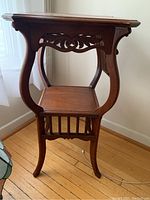 Side view of antique wooden plant table showing curved legs and carved side ornamentation.
