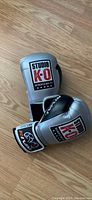 Pair of silver and black Studio K-O boxing gloves positioned on wooden floor.