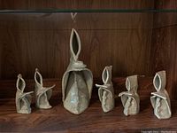 Six ceramic monk candle holders arranged on a wooden shelf, showing varying sizes and hooded monk shapes.